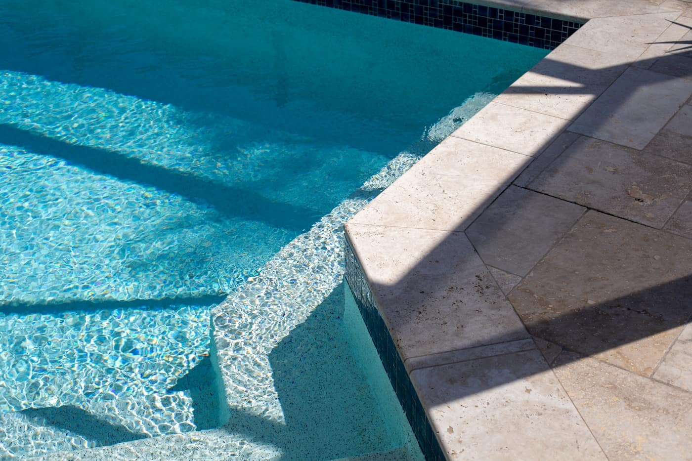 Sunlit pool corner with a wide paver deck and a tiled step-out edge