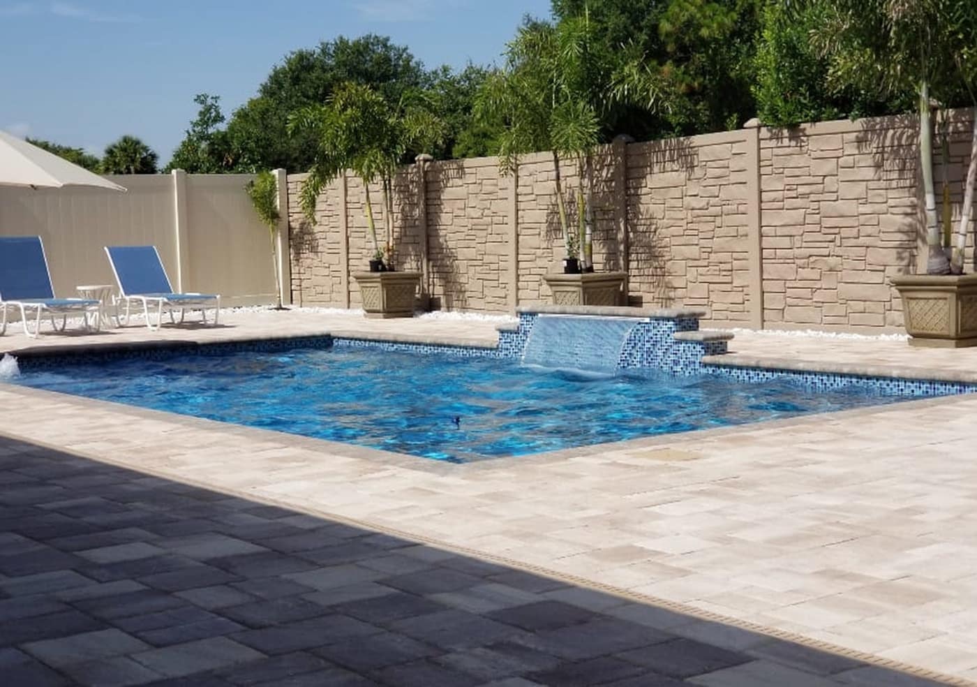 A backyard swimming pool with a water feature and a wide paver deck
