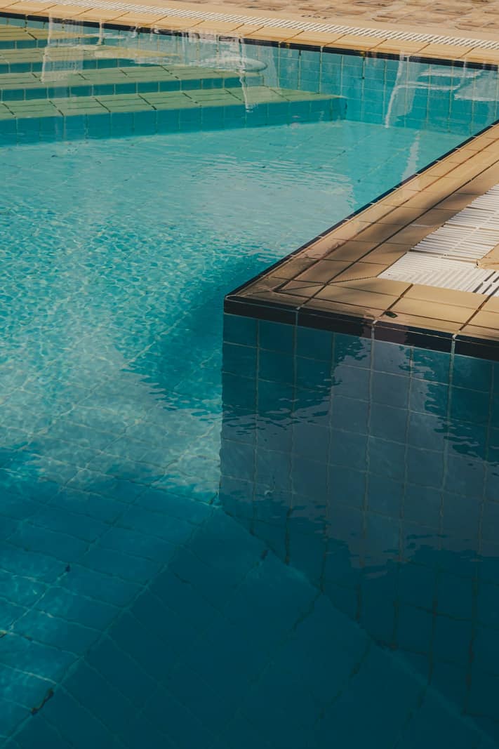 Corner of a swimming pool with glass waterline tile and a tiled coping edge over a stone deck